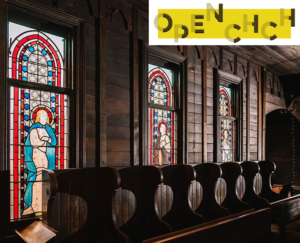 Image inside a church looking at wooden pews with dividers, wood panelling and stained glass windows.